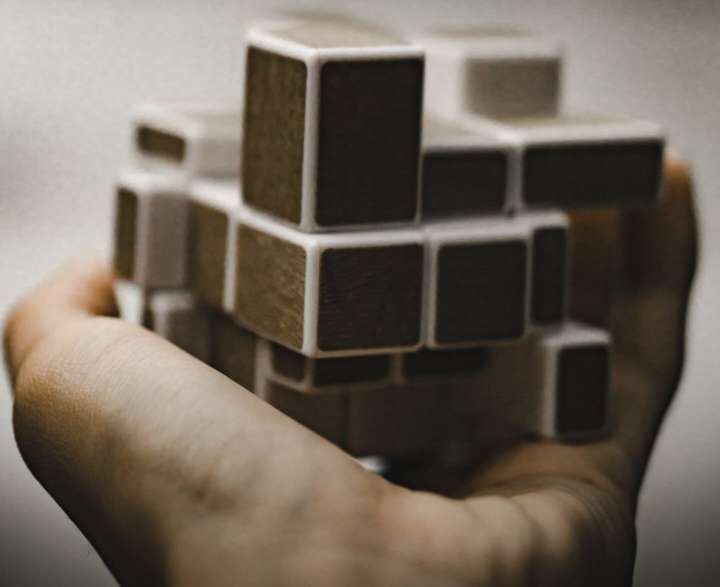 A close-up of a hand holding a complex wooden puzzle toy, symbolizing mental challenges.