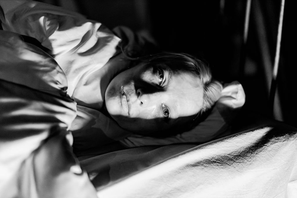Dramatic black and white portrait of a woman lying in bed with moody lighting.