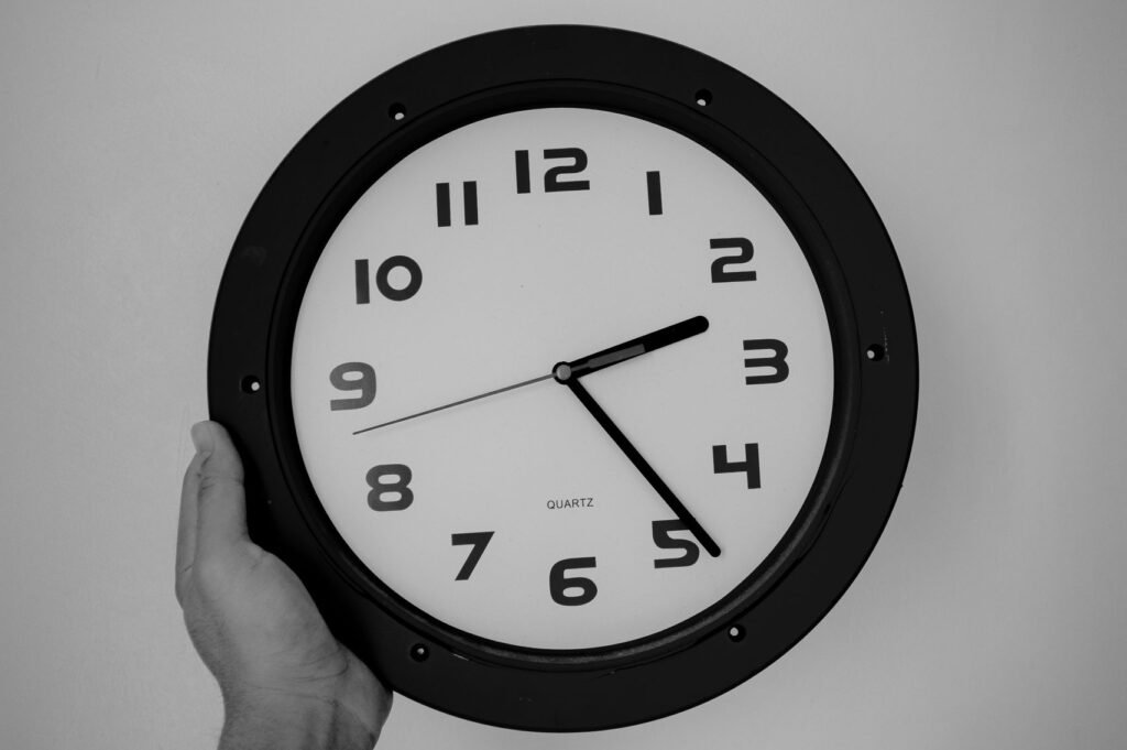 Minimalist black and white photo of a hand holding a wall clock, emphasizing time.